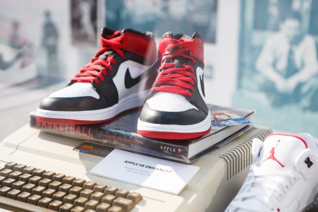 MOSKAVA-6 AUGUSTS, 2016: Reti Nike Air Force 1 basketbola čības melnā, baltā un sarkanā krāsā. Nike basketbola modes apavi stāv modes izstādē. Modes kāju apģērbi jauniešiem un Apple II pc - Image