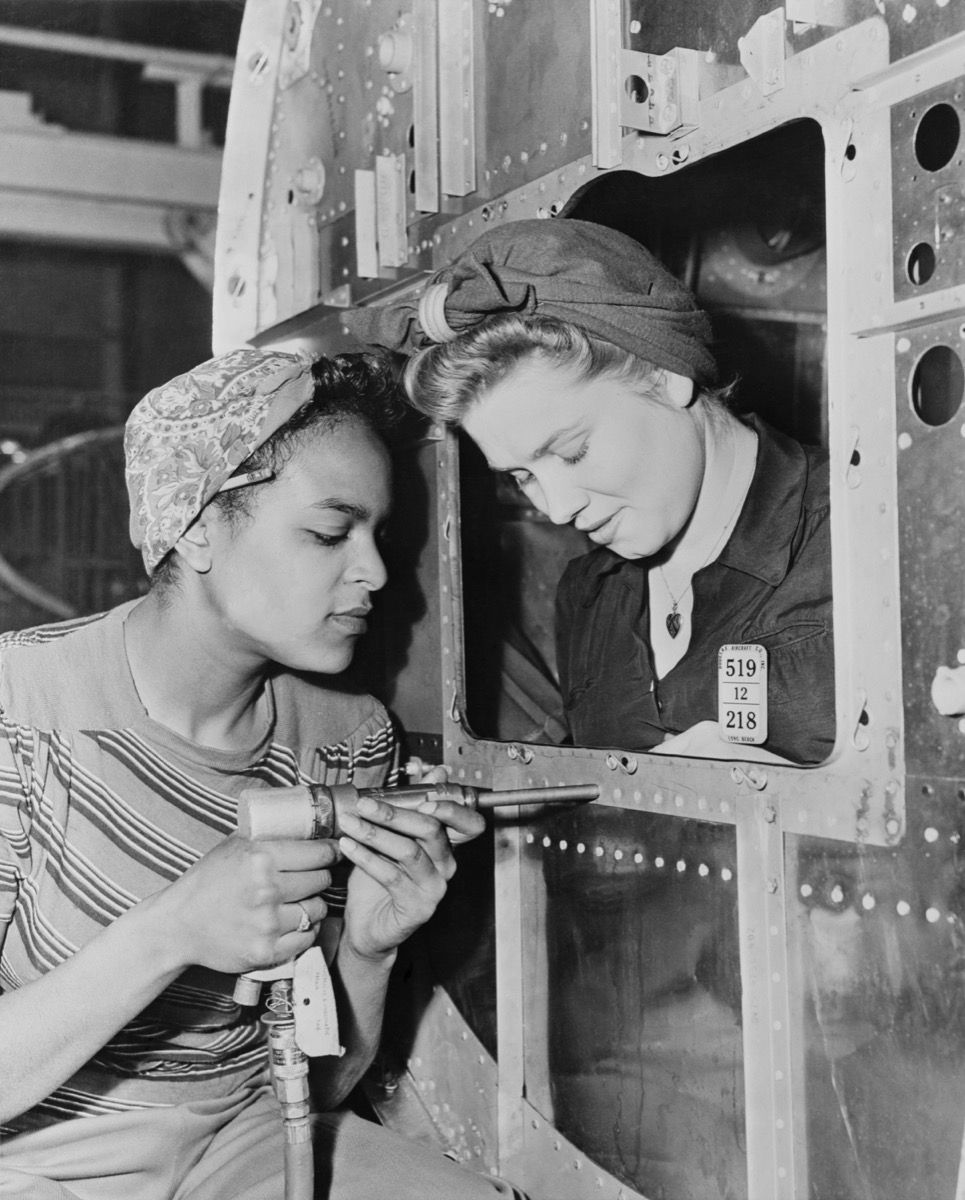 1940 m. dvi moterys, dirbančios ilgame paplūdimio fabrike, populiarios šukuosenos