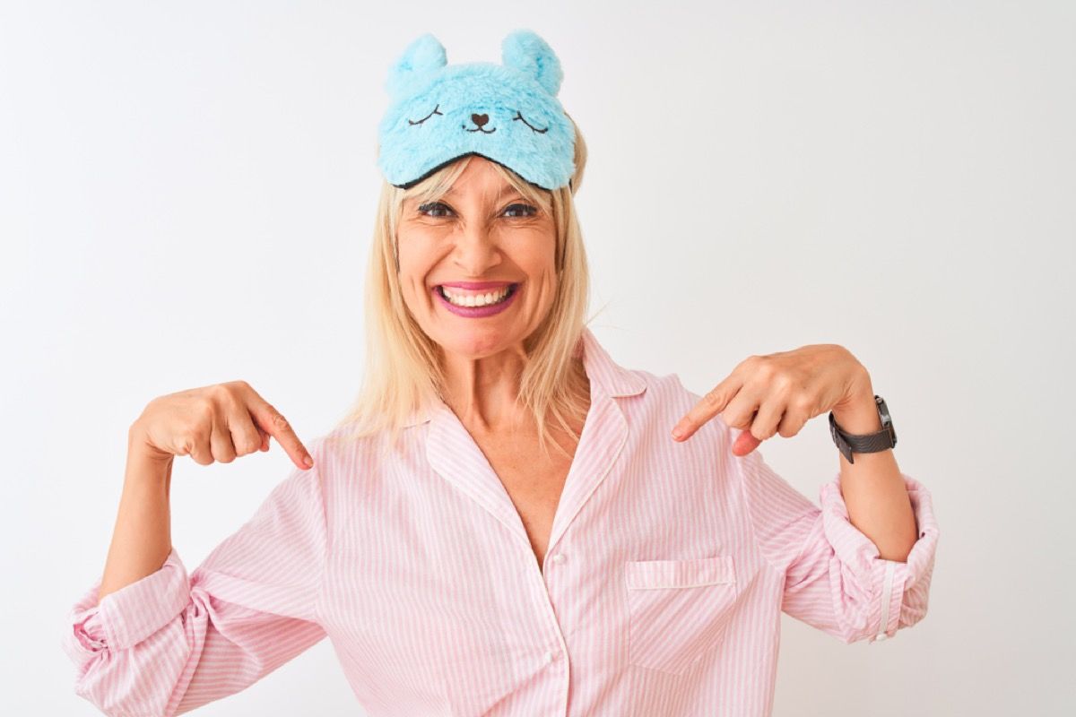 женщина средних лет улыбается в розовом халате и синей маске для глаз кролика