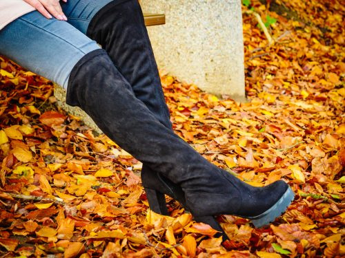   Жена отблизо's legs wearing jeans and black knee-high boots with orange leaves on the ground.