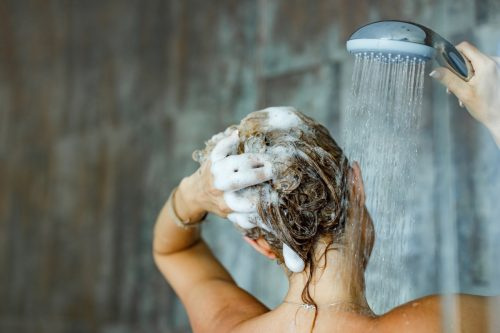   Bagsiden af ​​en kvinde, der vasker sit hår med en shampoo på badeværelset. Kopier plads.