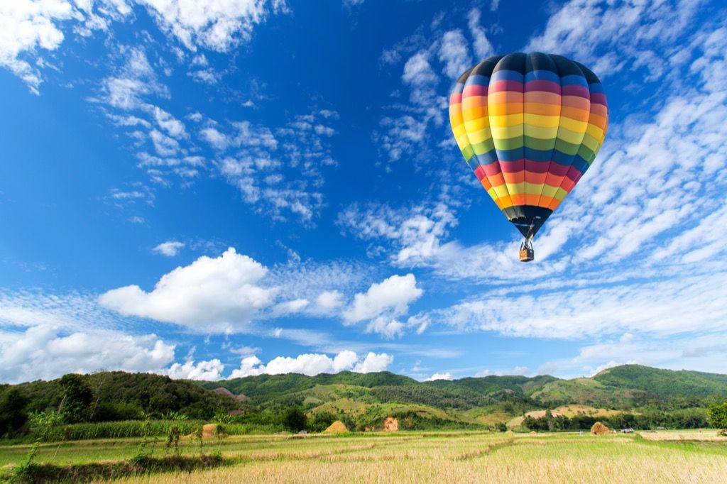 balonul cu aer cald de culoare curcubeu plutește în mijlocul norilor deasupra unei pășuni verzi, fapt despre statul Maryland