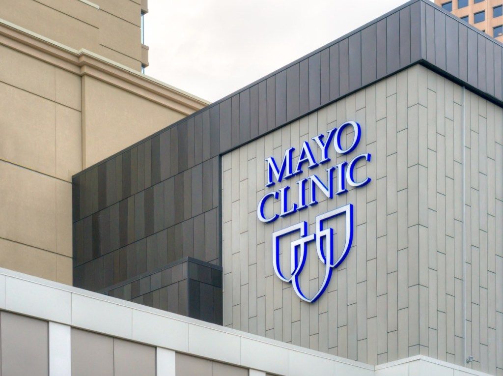 Mayo klīnikas ieeja un izkārtne baltas ēkas pusē, valsts fakts par Minesotu