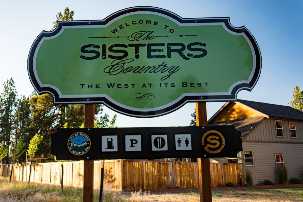 Biển báo chào mừng đến thị trấn Sisters Oregon vào lúc hoàng hôn vào mùa hè có nội dung The West At Its Best, sự thật của tiểu bang về oregon