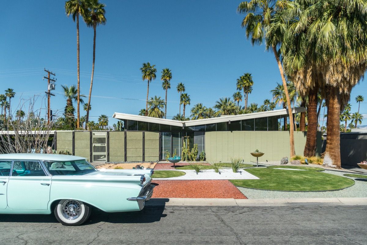 Coche azul retro de los años 50 estacionado fuera de una casa moderna de mediados de siglo con palmeras
