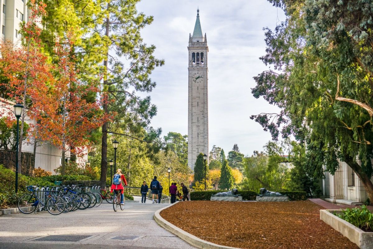 Estudiantes y visitantes caminando por el campus en un soleado día de otoño Sather Tower en el fondo