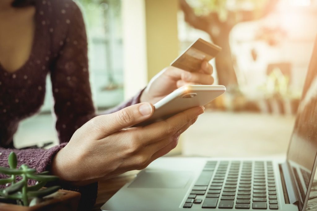 Mujer sentada frente a una computadora portátil con una tarjeta de crédito para comprar algo en su teléfono inteligente