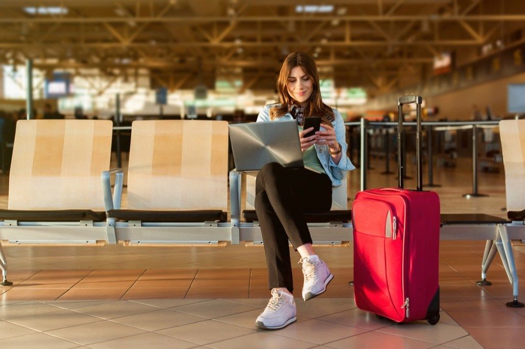 Mujer sentada en el aeropuerto esperando para viajar reservando vuelos baratos