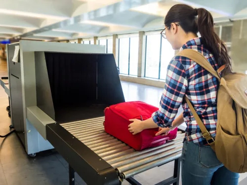   عورت ہوائی اڈے کے سیکیورٹی چیک کے ذریعے اپنا بیگ ڈال رہی ہے۔