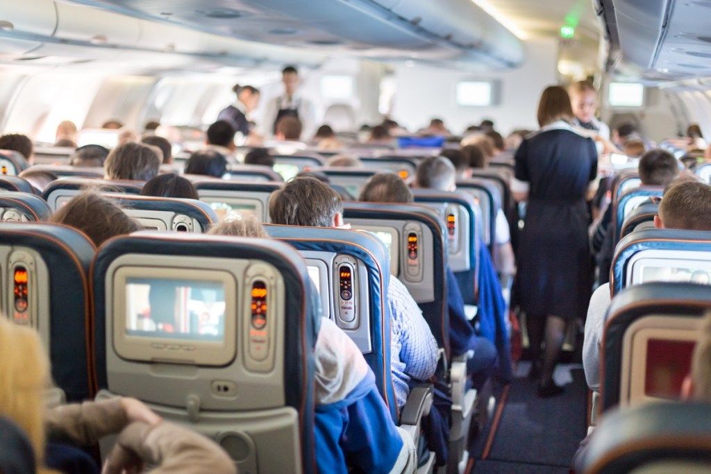 o stewardesă merge pe culoarul unui avion aglomerat