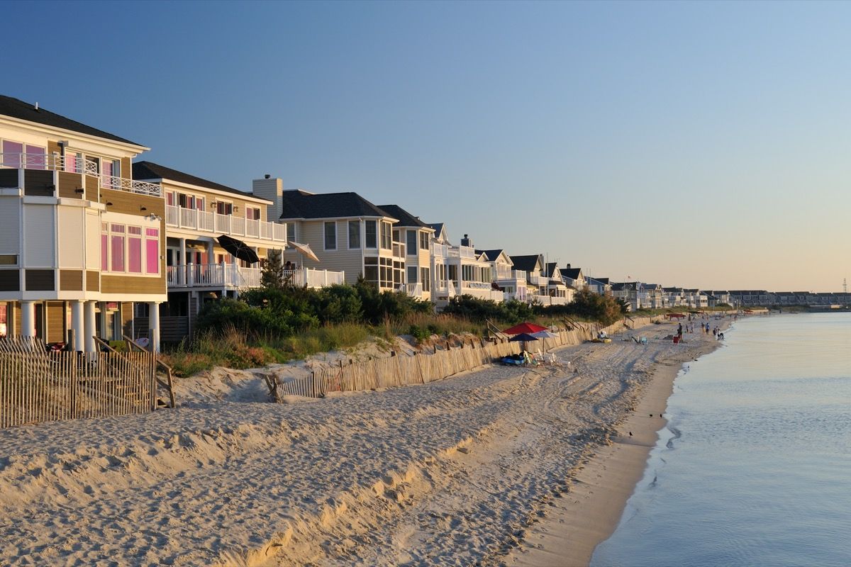 Prístinas casas de playa y villas de lujo con gente disfrutando de actividades en la playa en el fondo en el cabo Henlopen de Delaware, donde miles de visitantes vienen a disfrutar de la natación en el océano y tomar el sol durante el verano.