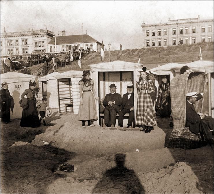 Foto de época de un grupo de personas sentadas en cabañas de playa