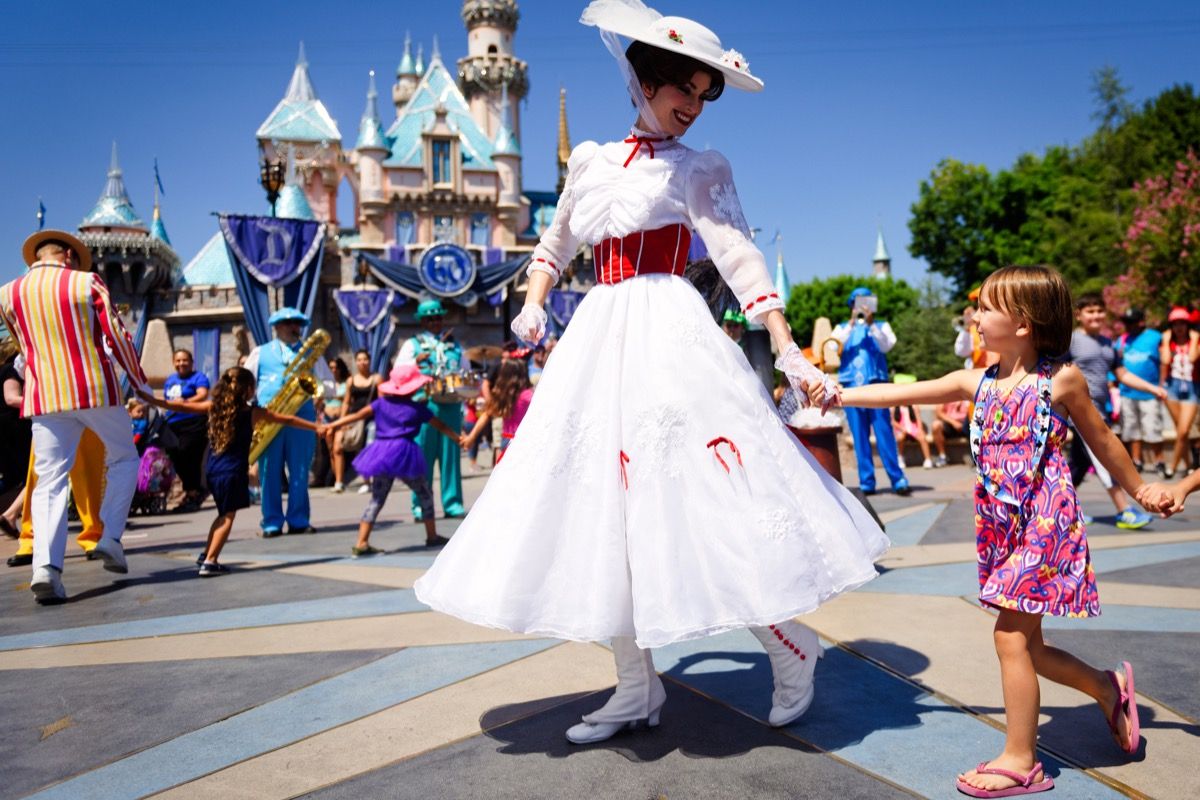 Mary Poppins smiler til et lite barn mens hun leder en linje med barn i sang og dans foran Askepott