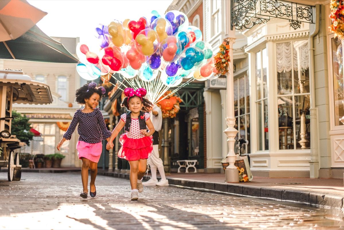 две момичета с уши на Мики Маус носят куп балони