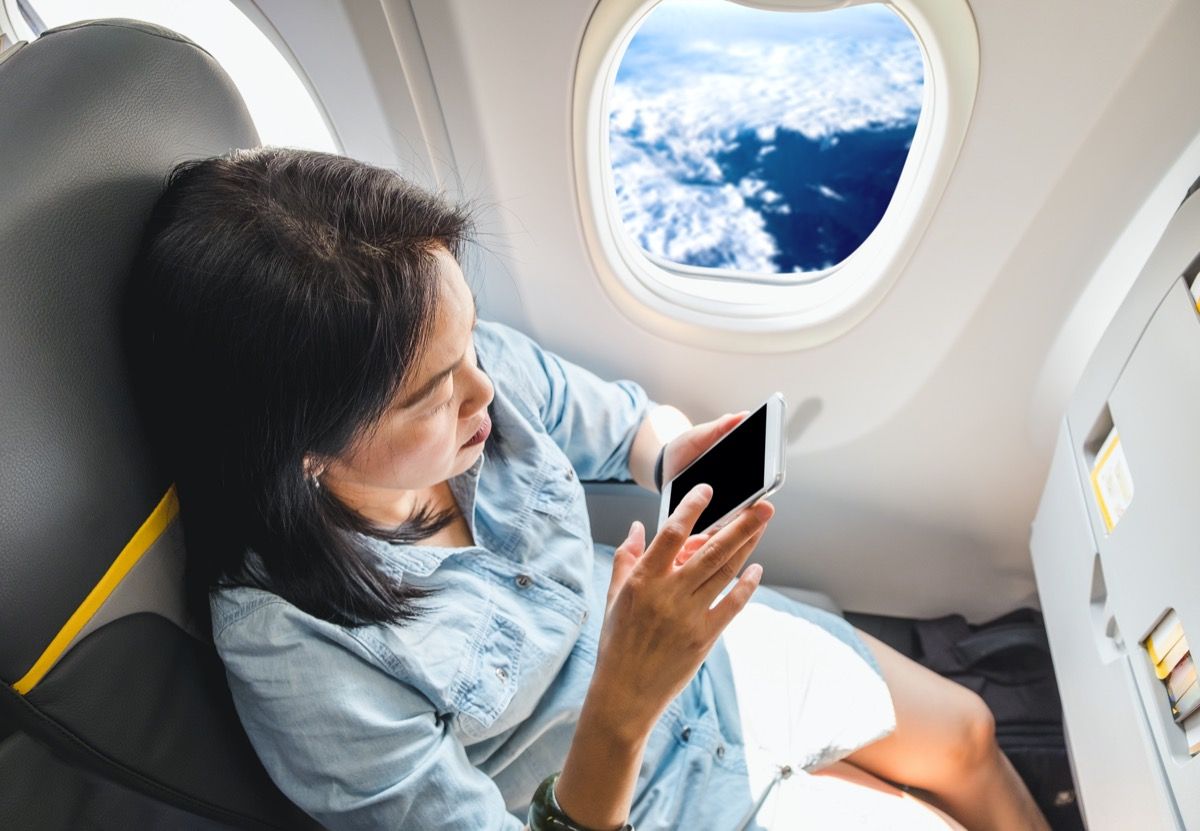 אישה אסייתית משתמשת בטלפון שלה במטוס