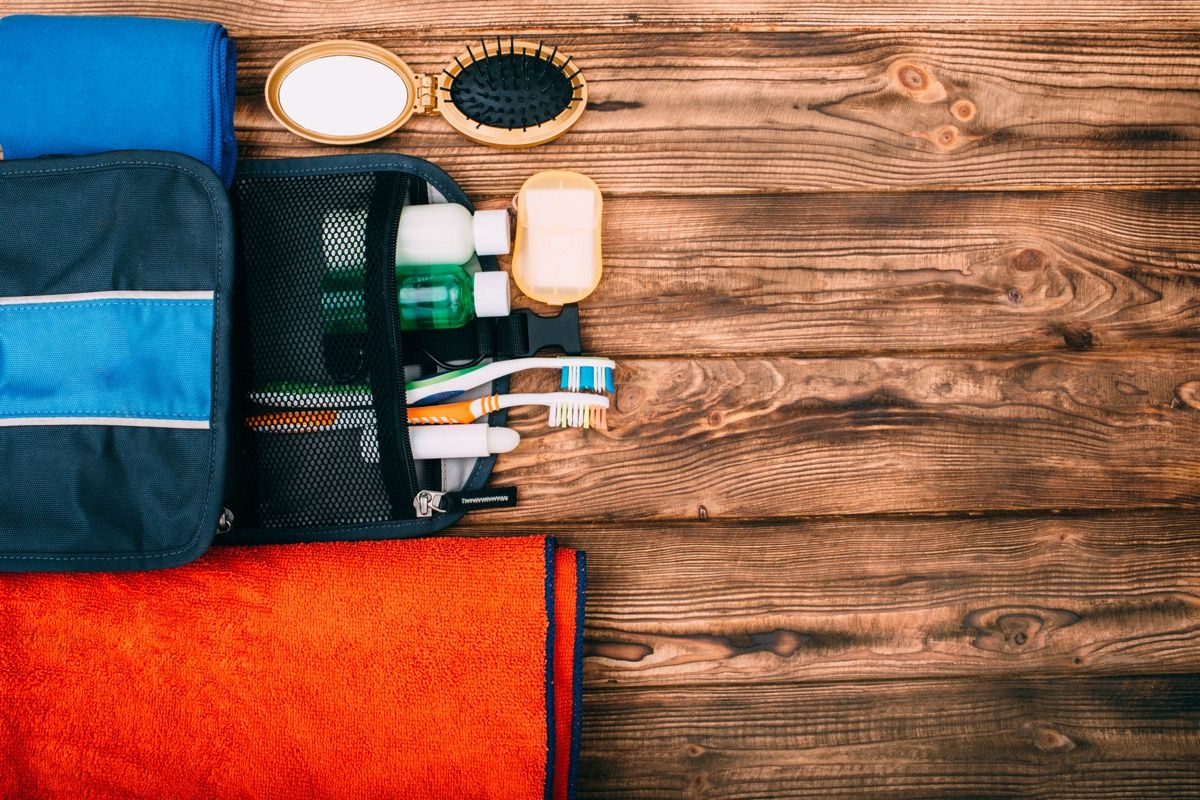 Изглед отгоре на комплект за хигиена по време на туризъм и пътуване на дървена маса с празно място. Артикулите включват кърпа, гребен, сапун, четки за зъби, шампоан.
