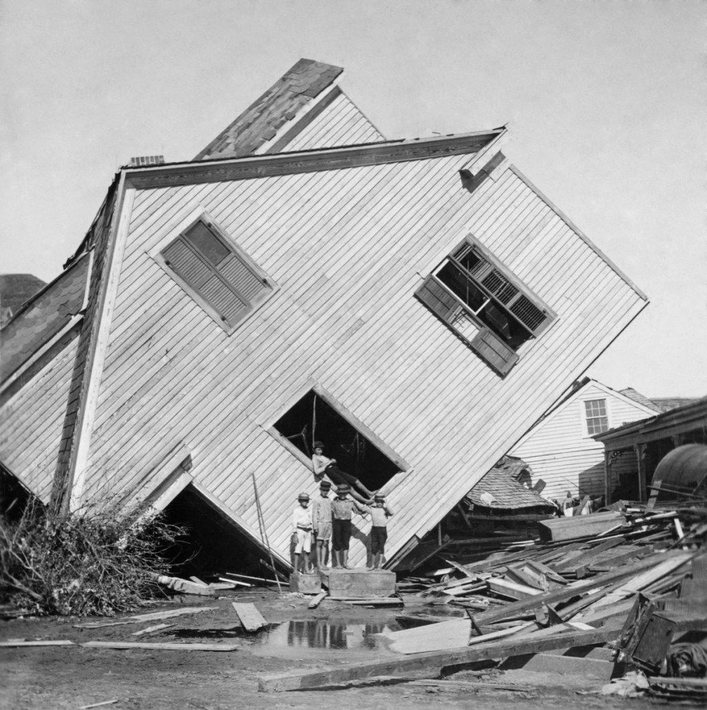 בית הוטה בצד לאחר התפרצות הסערה בגובה 15 מטר של הוריקן גלווסטון בספטמבר 1900. חמישה נערים מתייצבים מול הבית בשדרה N