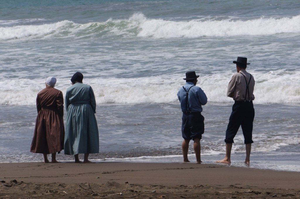 ארבעה אנשים אמישיים עומדים על החול מול החוף