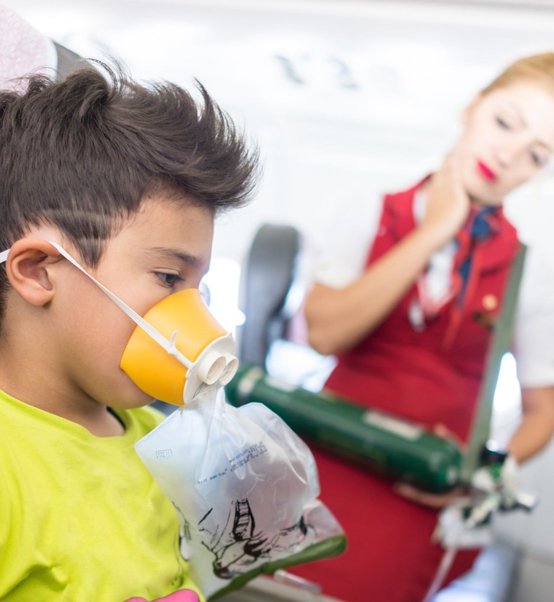 dječak u avionskom sjedalu s maskom za kisik dok gleda stjuardesa, iznervirana stjuardesa